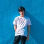 a young man leaning against a blue wall
